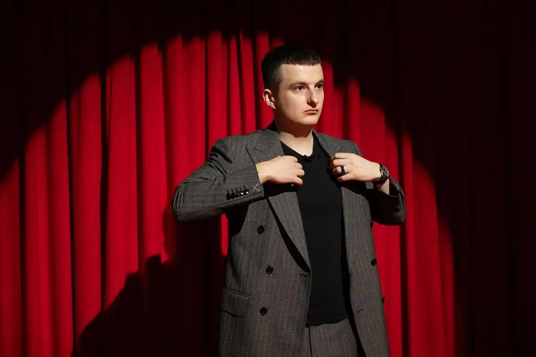 злой стример в костюме на фоне красного занавеса